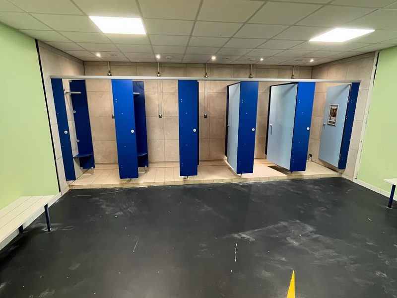 Vestiaire collectif terminé : cabines de douche installées, plafond démontable et éclairage intégré